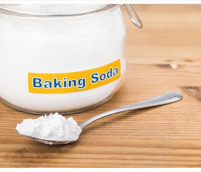 A jar with the word baking on it and in front of the jar there is a spoon with baking soda.